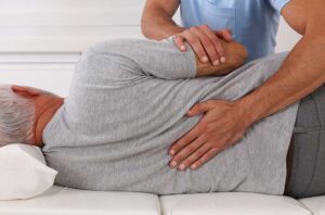 A chiropractor demonstrates a spinal adjustment while a physical therapist observes in a clinical setting.