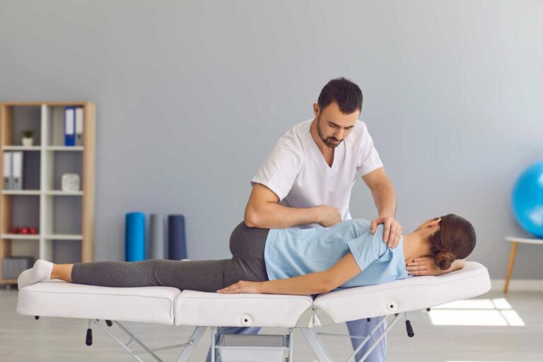 A person sitting on a yoga mat gently stretching their leg and knee with a calm indoor background.