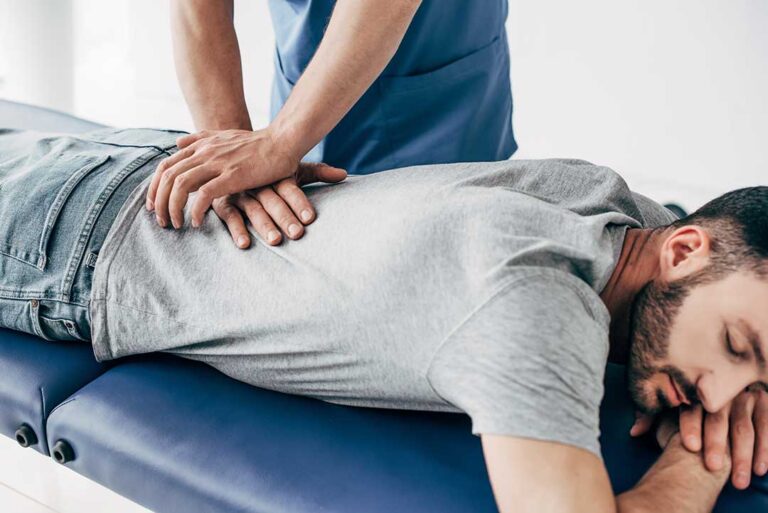 Person applying a towel-wrapped cold pack to the lower back while seated at home